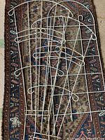 Three white painted metal garden trellis pieces laid out on a patterned rug, showing curved tops and circular decorative elements with vertical and horizontal metal rods