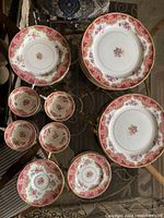 Top view of assorted fine china dishes including plates of various sizes, saucers and cups with pink and gold floral pattern.