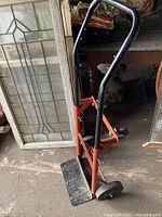 Side view of the orange metal moving dolly with black handle and platform base