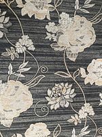 Close-up photo showing the pattern detail of cream and beige flowers with leaves on a black background with subtle stripes.