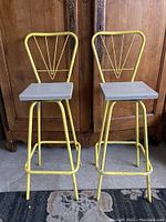 Pair of yellow metal swivel bar stools showing full view with wooden seats and distinct backrests