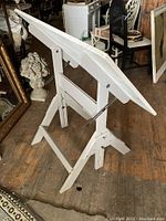 Photo of white adjustable wood drafting table with angled surface and sturdy base on wooden floor.