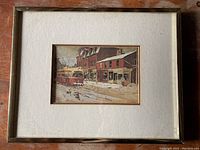 Framed print showing a winter scene with a Toronto streetcar and buildings, set within off-white matting and a gold-tone frame.