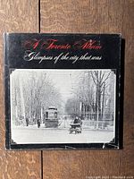 Photo of the book front dustcover with black background and a historic black and white photo showing a streetcar and a person with sled on a street with leafless trees.