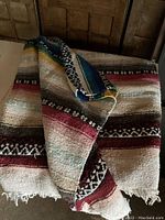 Photo showing folded vintage Mexican blanket with various colored stripes and fringed edges laid out against wooden background.