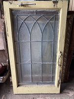 Full view of vintage lead glass window showing arch design, yellow wooden frame, and metal latch hardware.