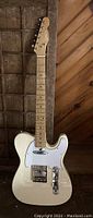 Full front view of cream-finish electric guitar leaning against wooden panel