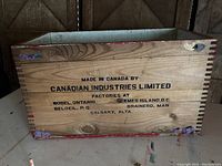 Front view of wood crate showing natural wood side with printed manufacturing details in black text