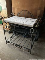 Full view of the wrought iron wine rack table with ceramic tiled top and brass accents on the sides.
