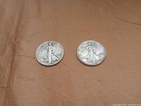 Two Walking Liberty half dollar coins placed on brown paper, front side visible.