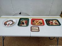 Top view showing all five tin trays with Coca-Cola designs arranged on two white folding tables.