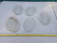 Five vintage clear glass sandwich plates laid out flat showing leaf embossed center and textured radiating lines, with tape measure for scale showing about 8 inches in length