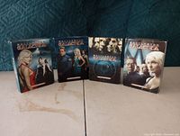 Four DVD box sets from Battlestar Galactica arranged in a row showing the front cover artwork.