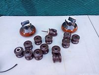 Photo showing two large brown-orange dome-shaped insulators with metal clamps and a group of 12 smaller brown ceramic spool-shaped insulators on a white surface with teal background.