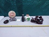 Photo of the full lot showing five distinct decorative Asian items arranged in a row with a measuring tape in front.