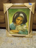 Framed painting showing a young girl holding a lamb, with original corner protection paper intact.