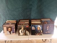 Four bins filled with vinyl records arranged on a table showing visible album covers including Merle Haggard, Robert Cray Band, and others.