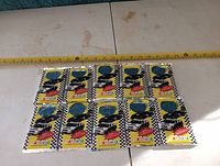 Twelve unopened NASCAR collector card packs laid out in a grid on a white surface with a measuring tape showing approximate dimensions.