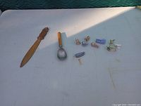 Lot items shown on a white surface include the carved wooden envelope opener, vintage ice cream scoop with wooden handle, and nine small Wade figurines.