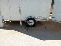 Full view of three items in lot: floor lamp, wrought iron stand, mosaic tile table, positioned outdoors on pavement near trailer.