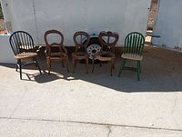 Five wooden chairs arranged outside, showing three antique wood chairs with carved backs in the center flanked by two painted modern wooden chairs in black and green.