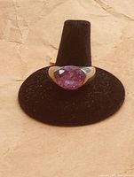 Front view of oval purple faceted stone set in sterling silver ring on black display stand.