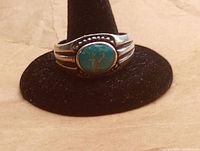Front view showing oval turquoise stone with brown veining set in sterling silver band with decorative dotted border.