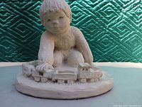 Front and slightly angled view of the statue showing the child playing with a train set on a round base.