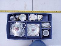 Porcelain tea set pieces packed inside original box showing teapot, cups, saucers, creamer, sugar bowl, all wrapped with tissue.