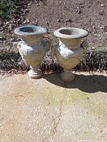 Two large vintage cement planters placed on concrete ground showing overall shape, size, and condition.
