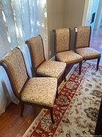 Four matching dining chairs arranged in a row against a window with a floral area rug
