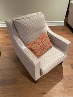 Front angle of the large plush armchair with beige patterned fabric and red/gold throw pillow