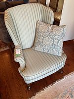 Front view of the wingback armchair with striped upholstery and damask throw pillow