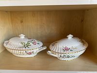 Pair of white porcelain lidded dishes with scalloped rims and floral hand-painted design. Both have handles and matching lids with shell-shaped knob.