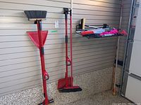 Two red brooms and one red dustpan with long handles against a wall