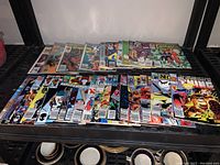 Photo of two rows of stacked comic books on a black shelf showing various Marvel and DC titles
