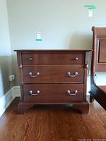 Front view of cherry wood dresser showing three drawers and hardware, placed on hardwood floor.