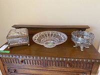 Photo showing the three pieces - rectangular crystal box with metal trim on left, large round glass dish center, and decorative glass bowl with feet on right.