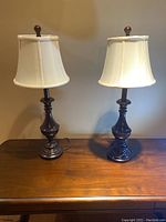 Two matching wood table lamps on a wooden surface against a wall, showing overall look and shade style.