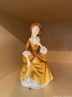 Front view of the Royal Doulton porcelain figurine showing the delicate facial details and front of the yellow dress with ruffled, dotted trims.