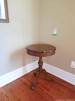 Wooden side table positioned in corner, showing full profile including the turned pedestal and legs.