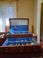 Two wooden cases opened showing multiple slots filled with silver plated cutlery arranged in blue felt lining.