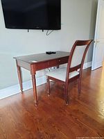 Table and chair set shown together in a room, displaying the table's wooden surface, drawer, and the chair's upholstery and wood finish.