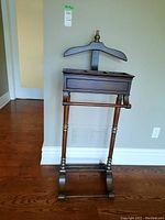 Front view of wood valet stand showing hanger, drawer, and feet.