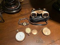Three pocket watches and Tasco opera glasses with leather case on wooden surface