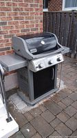 Weber Spirit natural gas barbecue grill outside against a brick wall with stone patio floor.