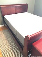 Front angle of a wood veneer sleigh bed with white mattress.
