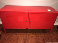 Front view of red metal storage cabinet with two locking doors, showing ventilation slats and key locks.