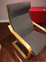 Side front angle of IKEA Poang chair showing light wood bentwood frame and stained gray upholstered seat and backrest.