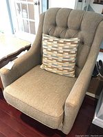 Front angle view of beige upholstered armchair with tufted back and patterned cushion.